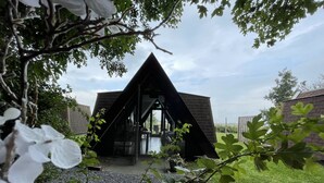A modern, triangular-shaped building with a glass entrance, surrounded by greenery and gravel. - Restinn Medemblik (Wieringerwerf)
