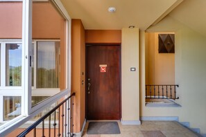 Une porte en bois avec un panneau indiquant «Interdiction de fumer », un escalier avec une rampe en métal et une vue sur l’extérieur à travers une porte vitrée.