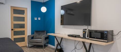 A modern room with a bed, a desk with a microwave, a chair, and a TV on the wall.