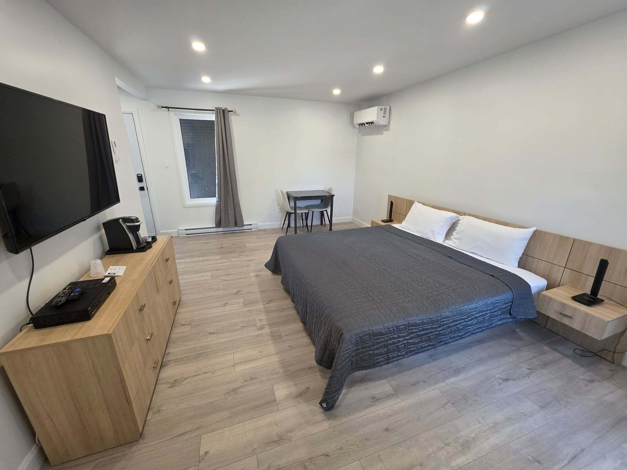 A modern hotel room with a bed, bedside table, TV, and a desk with a chair.