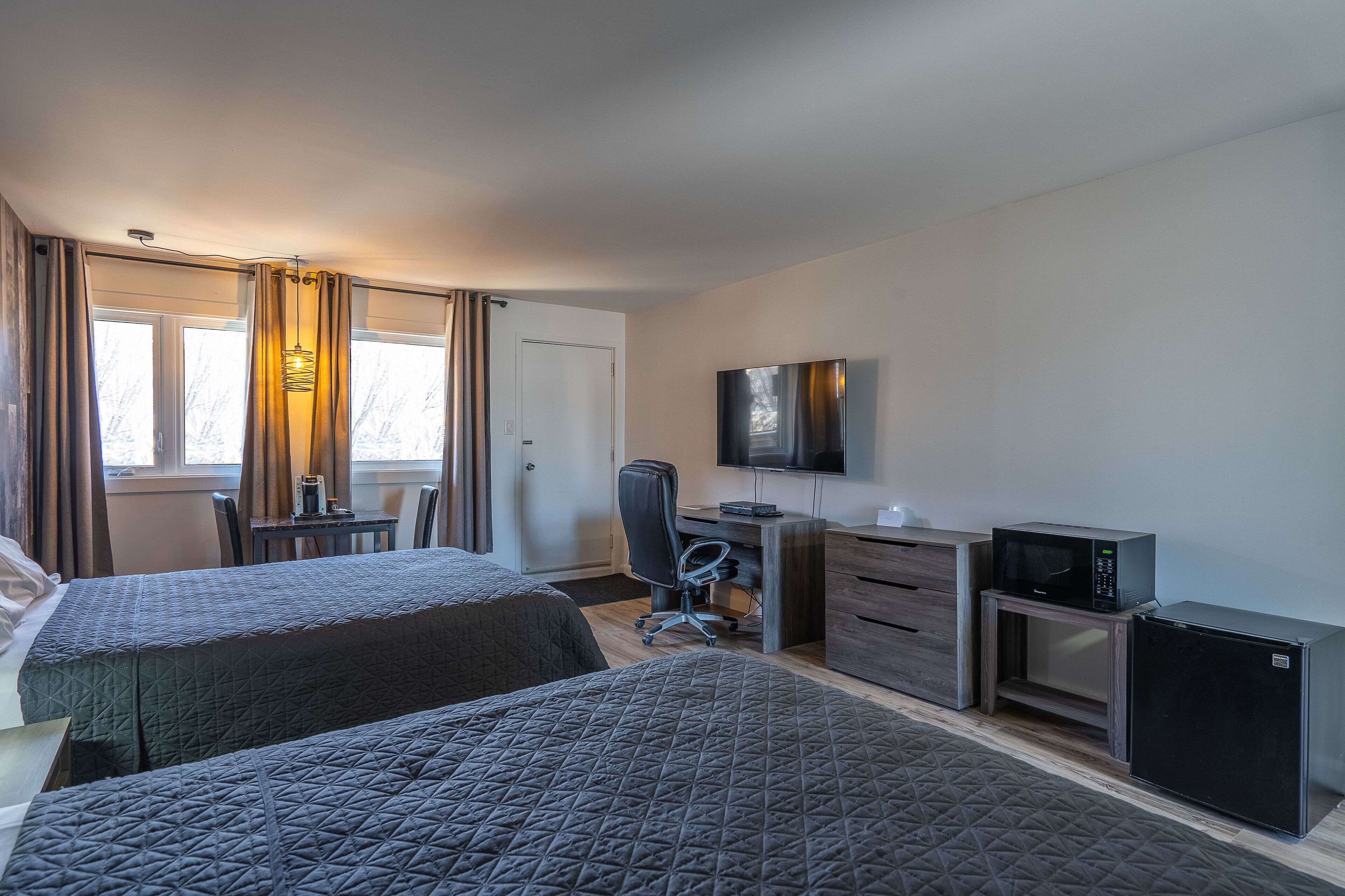 A hotel room with two beds, a desk, a chair, a television, a microwave, and a refrigerator.