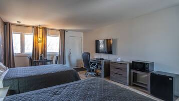 A hotel room with two beds, a desk, a chair, a television, a microwave, and a refrigerator.