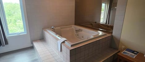 A modern bathroom with a large bathtub, a shower area, and a window providing natural light.