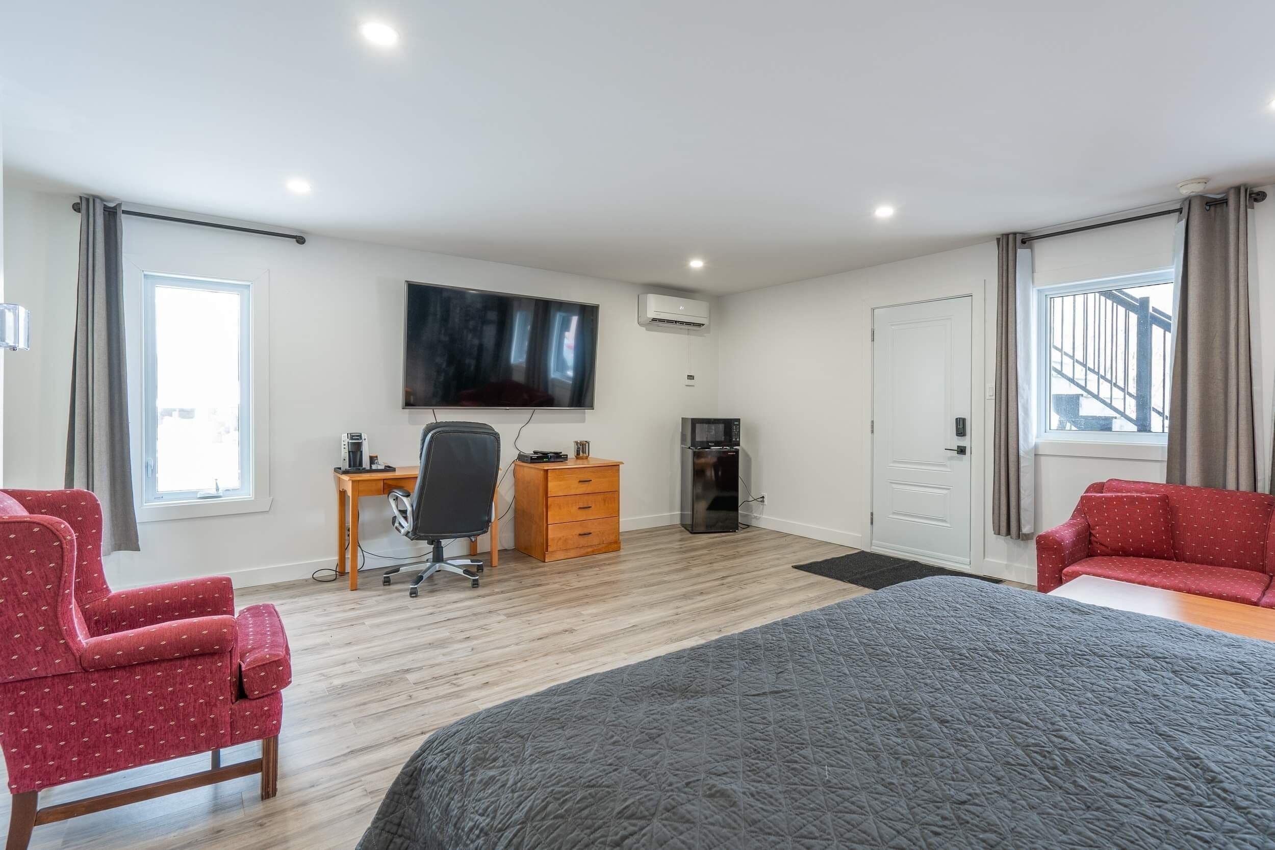 Une chambre d’hôtel moderne avec un grand lit, un bureau avec une chaise, un téléviseur fixé au mur et un canapé rouge.