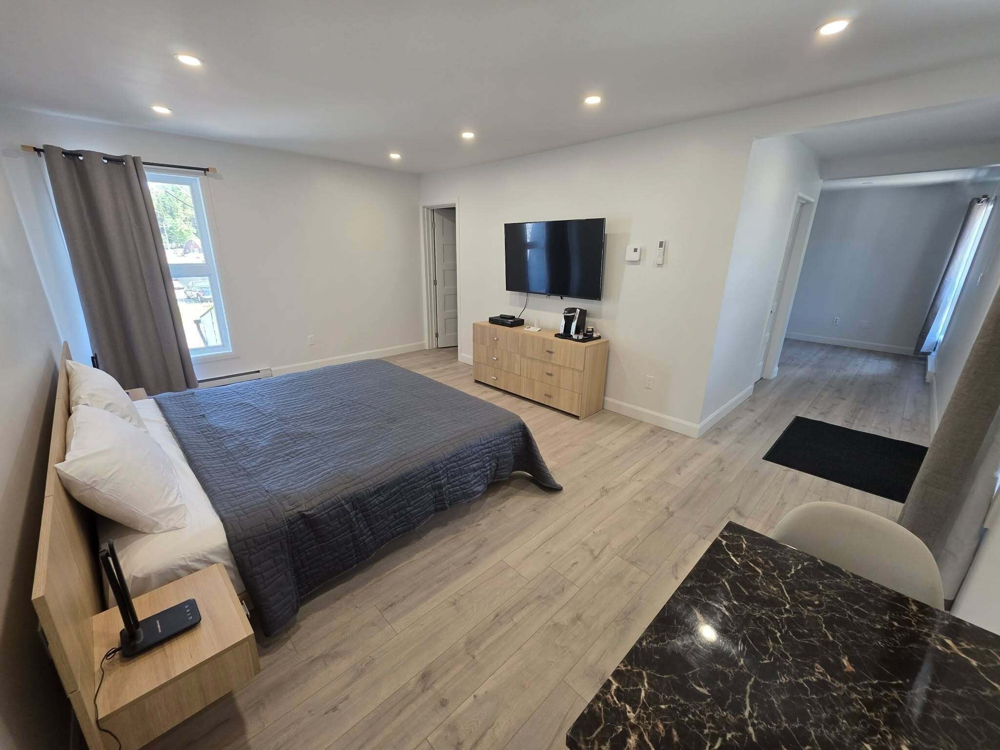 Quarto moderno com cama, TV, cómoda de madeira e mesa de mármore.