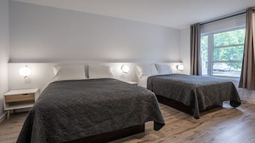 A hotel room with two beds, wooden flooring, and a window with curtains.