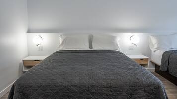 A modern bedroom with a large bed, bedside tables, and wall-mounted lighting.