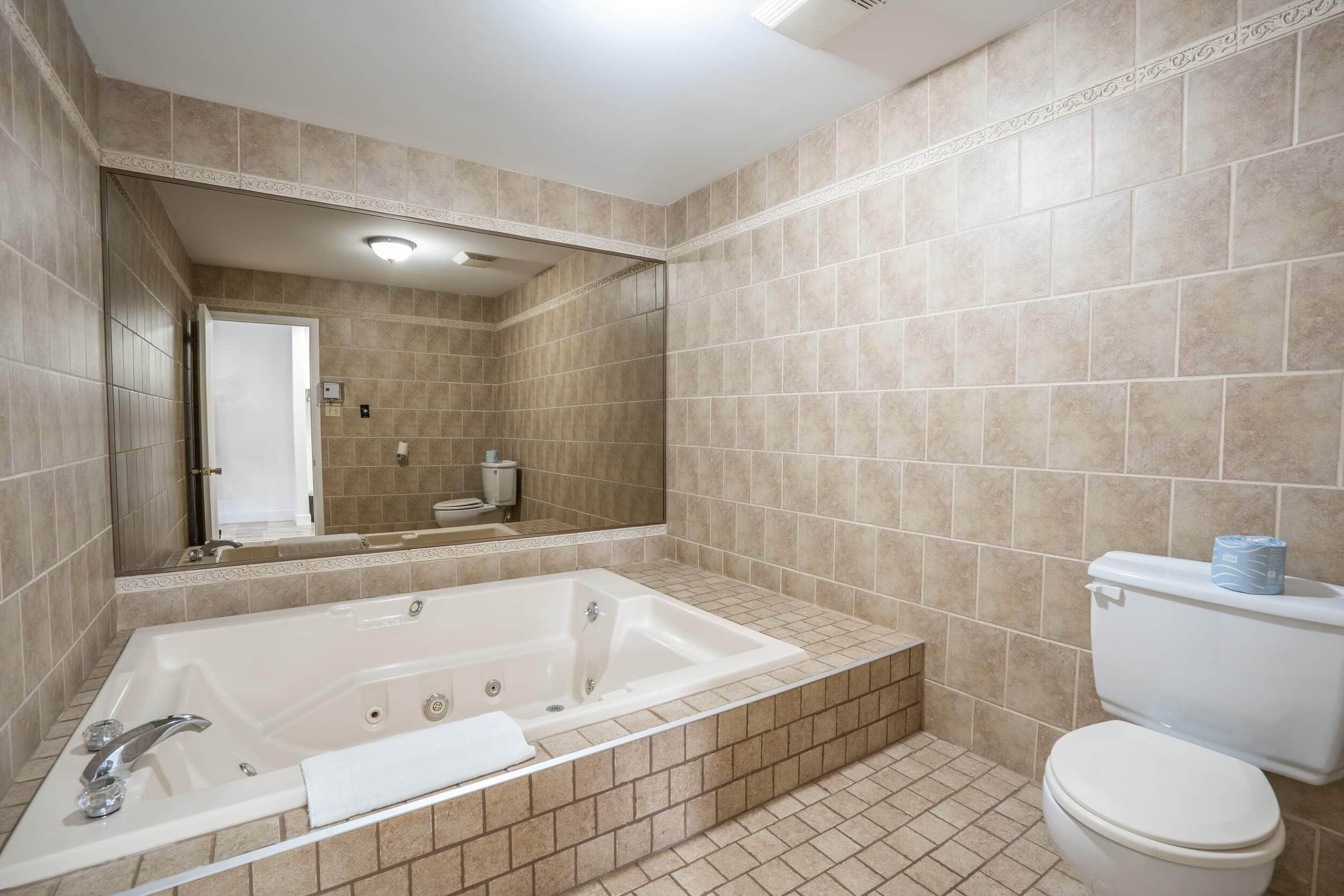 A bathroom with a large bathtub, a toilet, and a mirror.