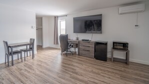 A modern living room with a wooden floor, a dining table with chairs, a TV, a refrigerator, a microwave, and a small table. - Le 2020 (La Malbaie)