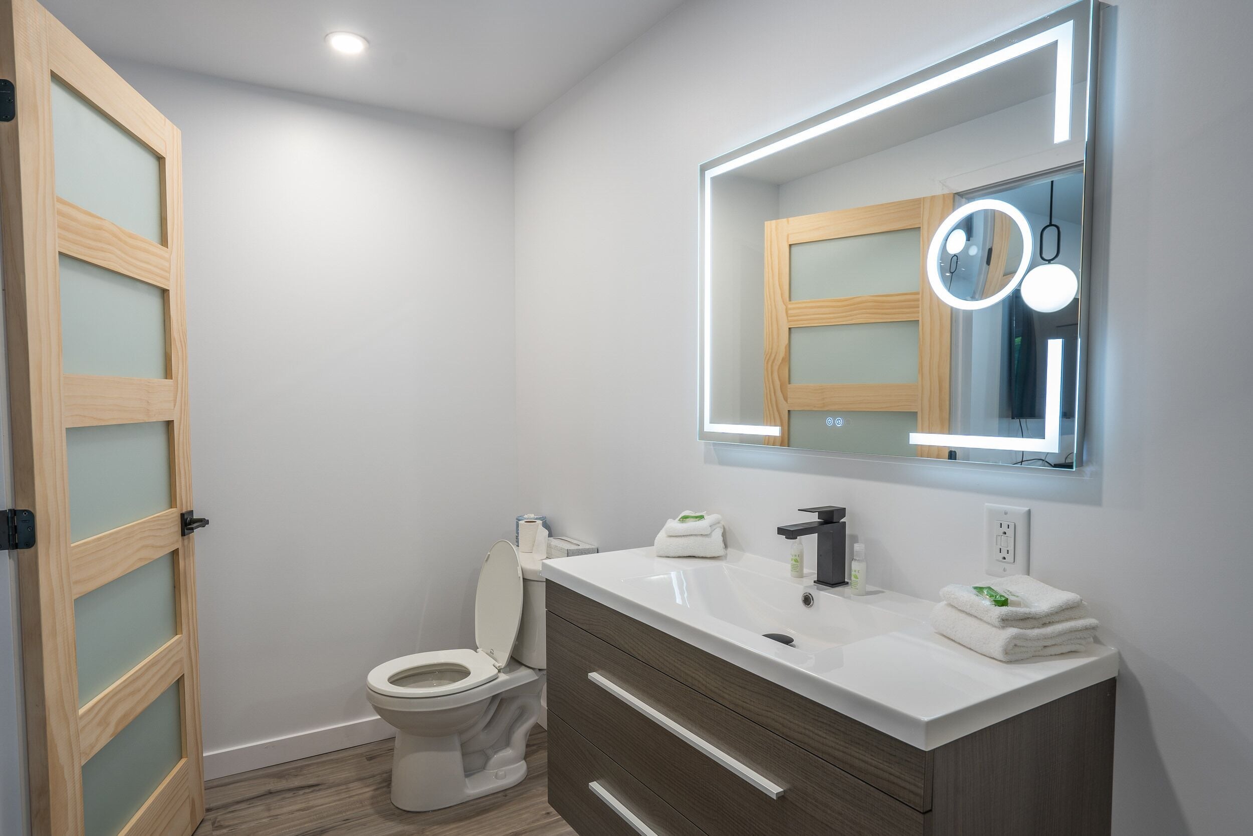 A modern bathroom with a toilet, vanity, and mirror.