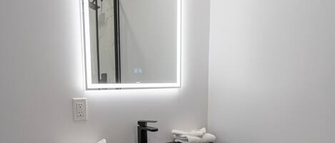 A modern bathroom with a black sink, wooden cabinet, and a mirror with integrated lighting.