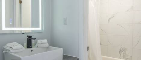 A modern bathroom with a white sink, mirror, and shower.