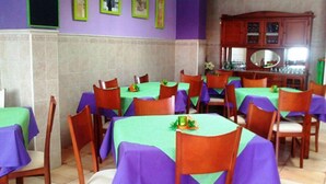 Un comedor con mesas cubiertas con manteles verdes y púrpuras, sillas de madera y un aparador de madera con un espejo.