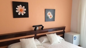 Una cama doble con sábanas blancas, un cabecero de madera y dos cuadros de flores colgados en la pared.