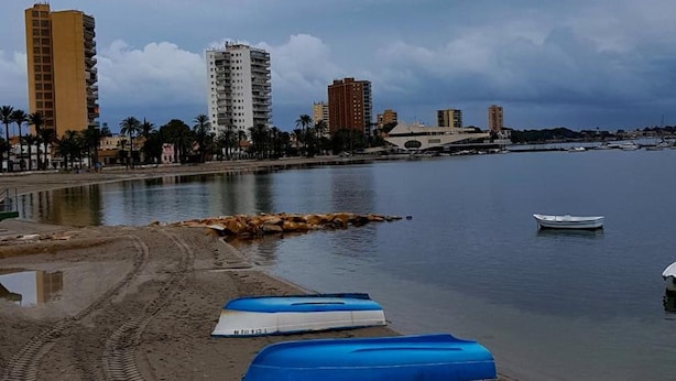 Una playa con huellas que llevan al agua, un bote y edificios al fondo.