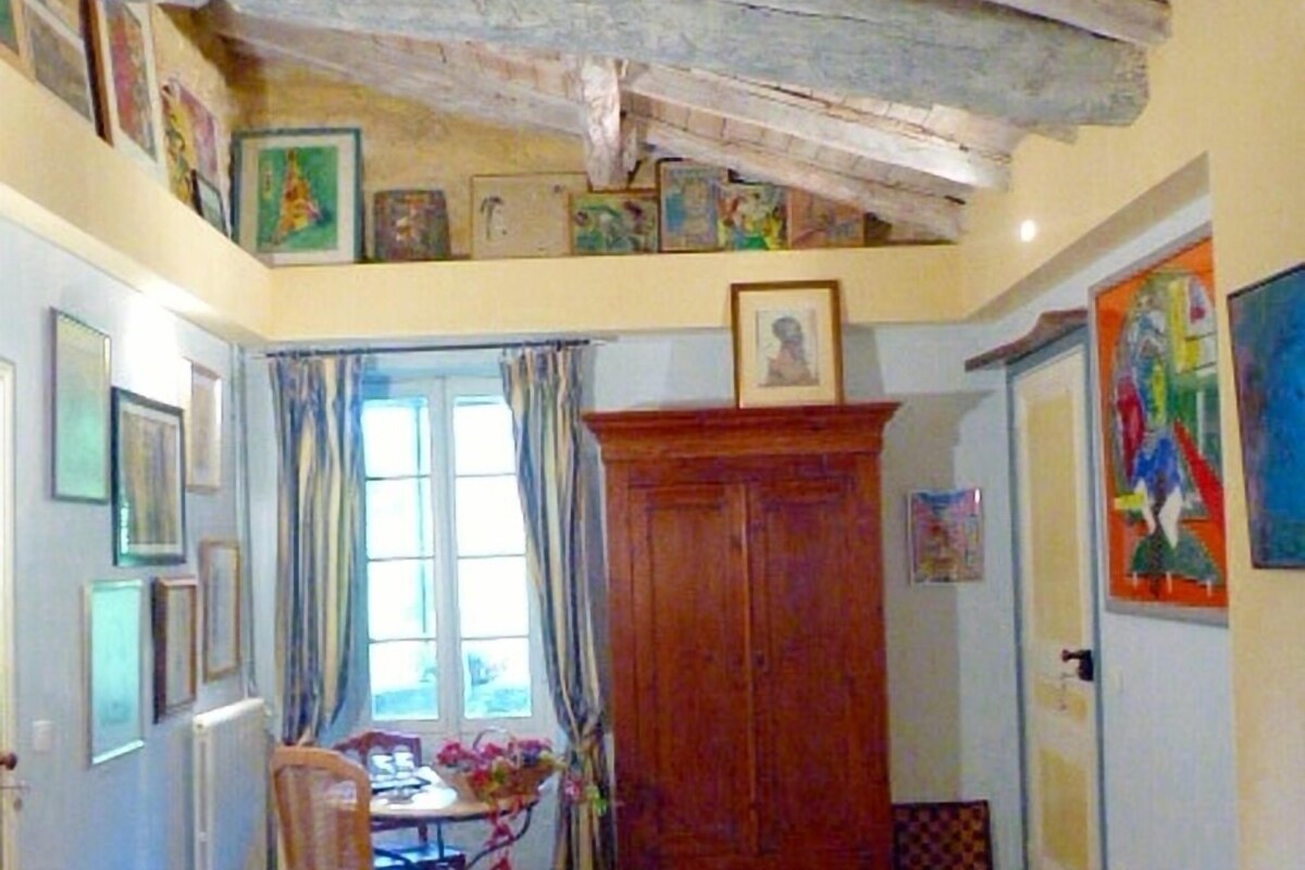 A room with wooden beams on the ceiling, a large rug, a wooden cabinet, and various framed pictures on the walls.