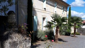 A historic building with a stone facade, a paved driveway, and lush greenery including a palm tree and flowering plants. - Domaine Mongiron (Nerigean)