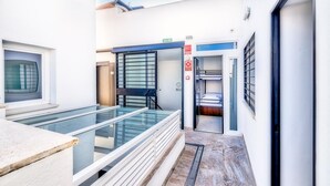 A modern hotel corridor with a glass railing, a door leading to a room with a bunk bed, and a sign indicating a fire exit. - Hostel A2C - Adults Only (Seville)