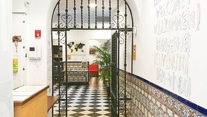 A hotel lobby with a check-in counter, a tiled floor, and a wall with multilingual welcome signs. - Hostel A2C - Adults Only (Seville)