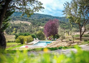 Una piscina con sillas de descanso, rodeada de árboles y colinas al fondo.