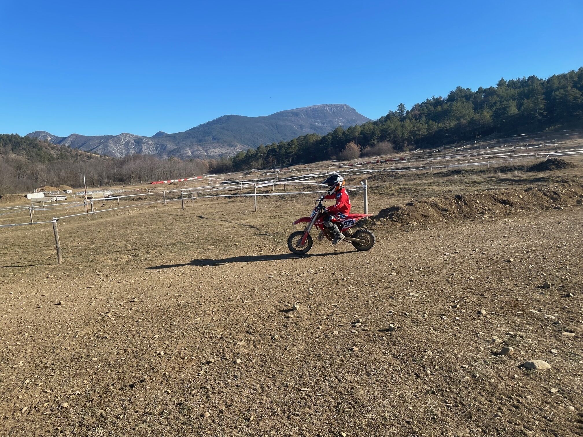 Un camino de tierra con un motociclista en una moto roja.
