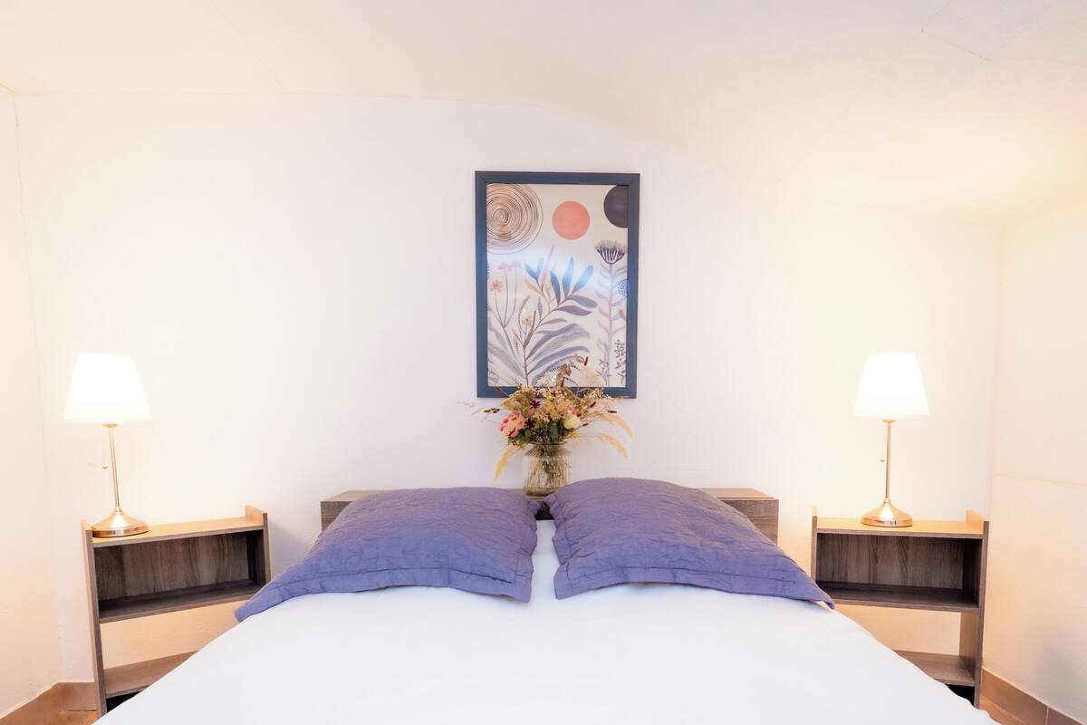 A neatly made bed with two pillows, a wall-mounted painting, and two bedside lamps.