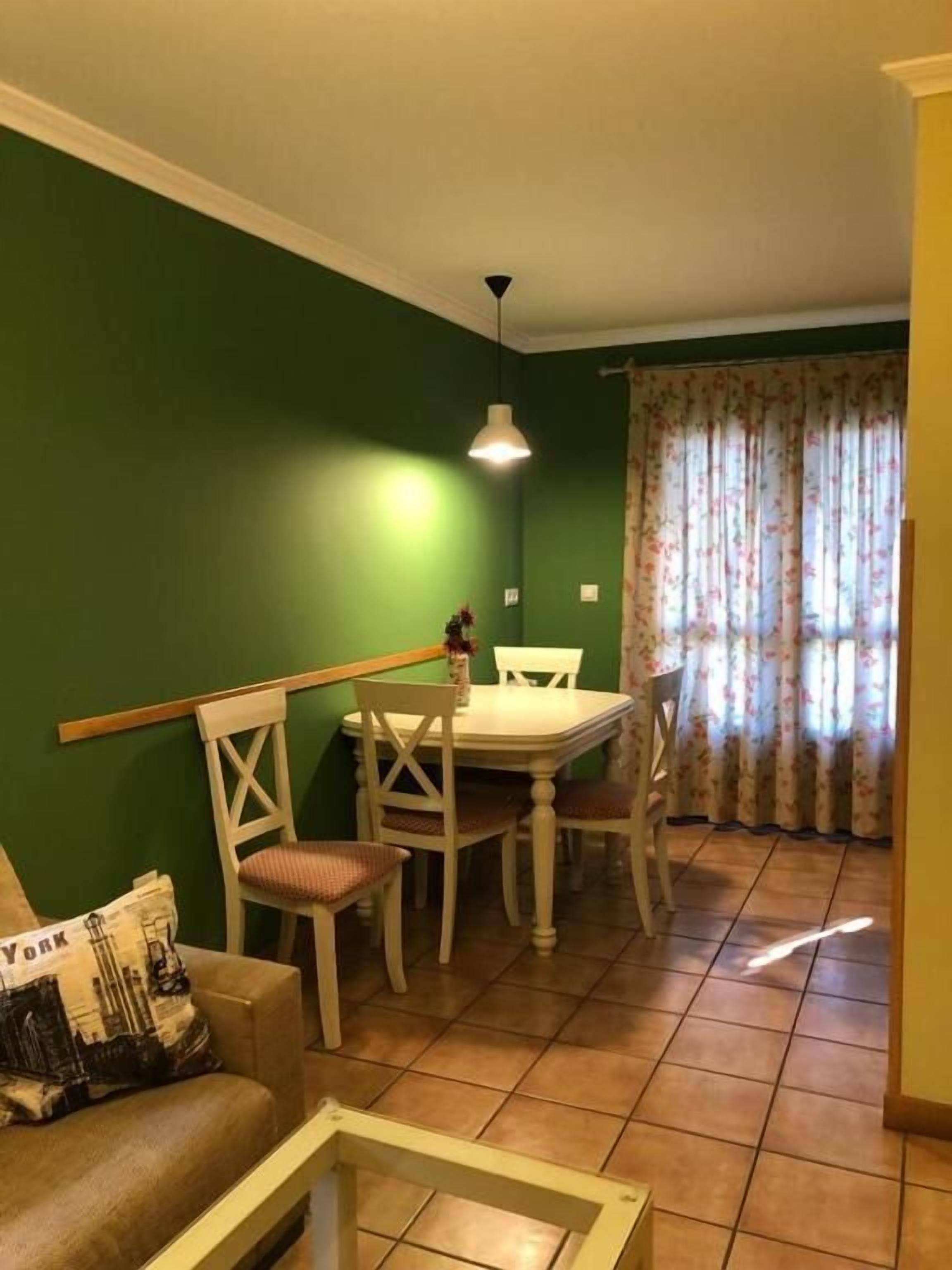 A dining area with a table and chairs, a hanging light fixture, and a window with floral curtains.