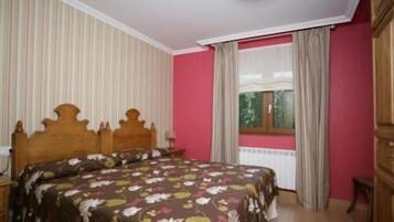 Un dormitorio con cama de madera, ventana con cortinas y radiador.