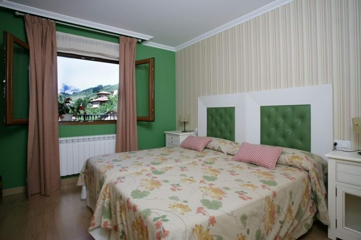 Une chambre avec un grand lit, des murs verts, une fenêtre avec des rideaux et une vue sur une montagne.