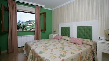 Quarto com cama grande, paredes verdes, janela com cortinas e vista para uma montanha.