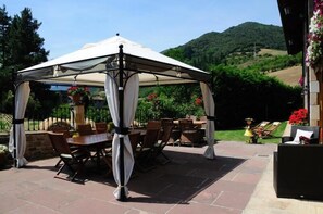 A covered patio area with a table and chairs, surrounded by a stone wall and a view of a hilly landscape. - Posada El Corcal De Liébana (Cillorigo de Liebana)