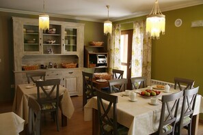 A dining area with a table set for four, surrounded by wooden chairs, a buffet cabinet with glass doors, and two chandeliers. - Posada El Corcal De Liébana (Cillorigo de Liebana)