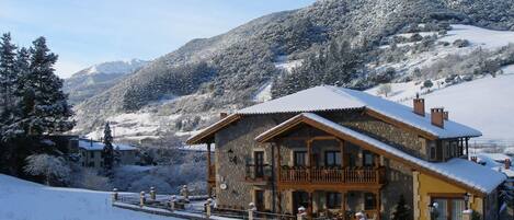 Un edificio de estilo chalet con balcón, rodeado de montañas y árboles nevados.
