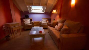 A cozy living room with a sofa, two armchairs, a coffee table, a TV, and a skylight.