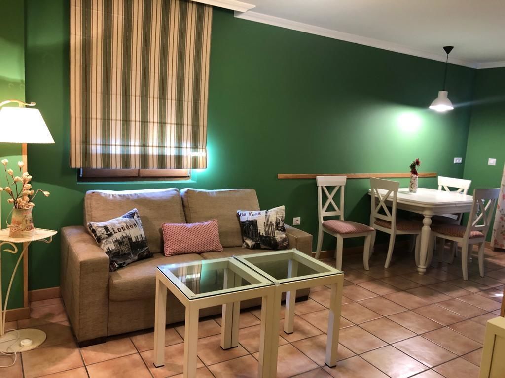 Una sala de estar con un sofá, una mesa de centro de vidrio, una mesa de comedor con sillas y una lámpara.