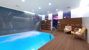 A pool area with a wooden deck, a water slide, and a bench with towels. - Kores Boutique Hotel & Spa (Zagori)