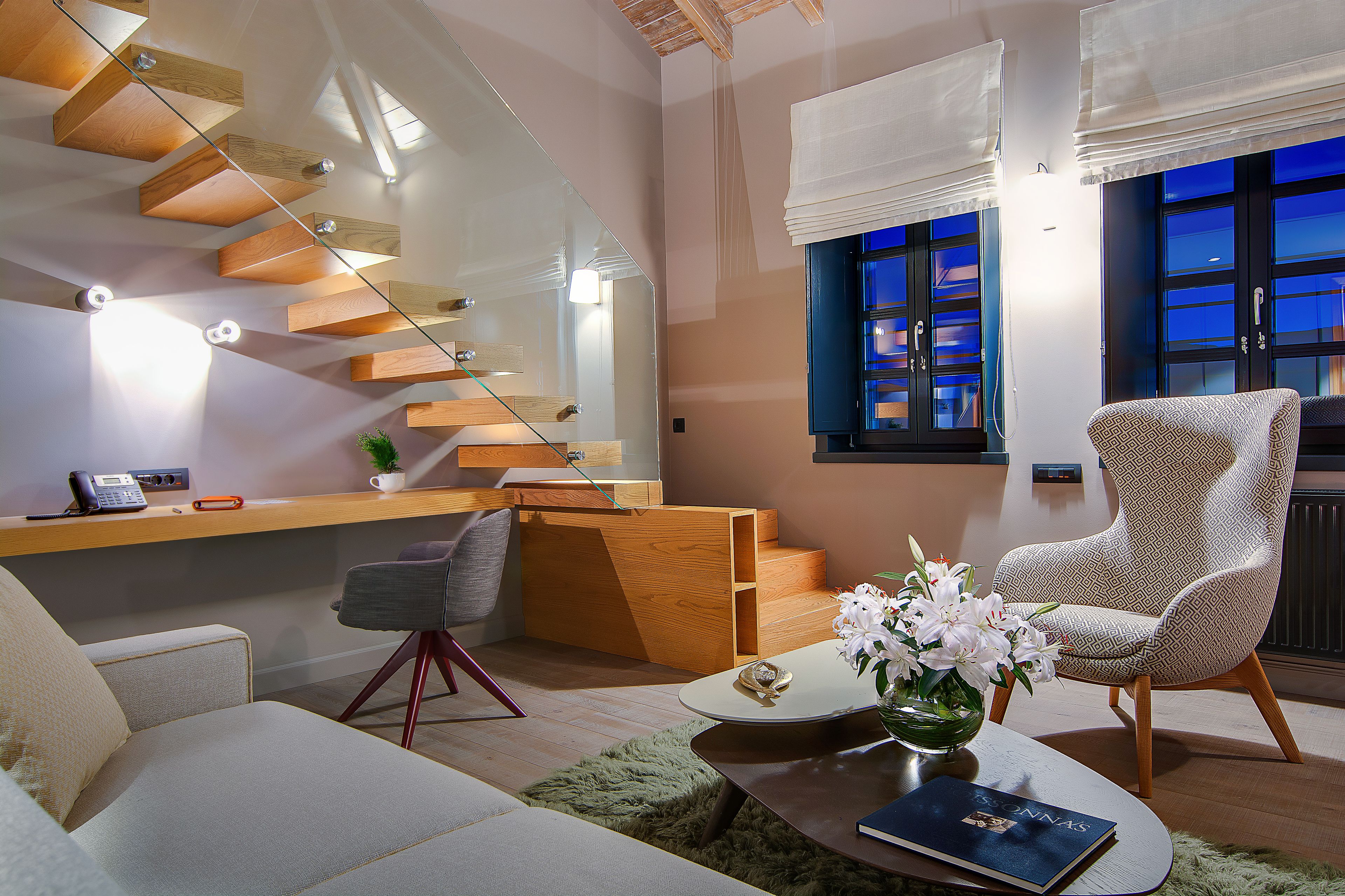 A modern living room with a staircase, a comfortable sofa, a coffee table, and a patterned armchair.