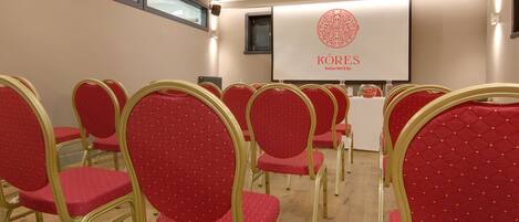 A conference room with rows of red chairs and a podium with a screen displaying the logo and name of Kores Boutique Hotel & Spa.