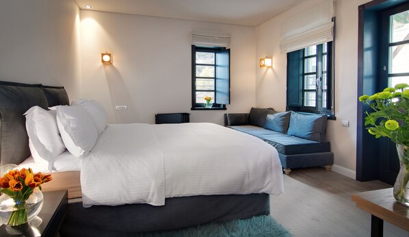 A modern bedroom with a large bed, a bedside table with a vase of flowers, a window with a view, and a blue door.