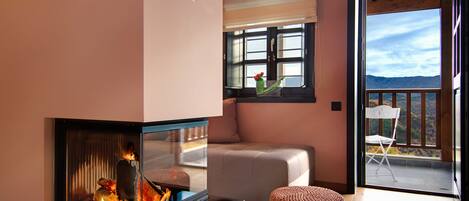 Un salón acogedor con chimenea, un sofá cómodo y vistas al exterior a través de un ventanal grande.