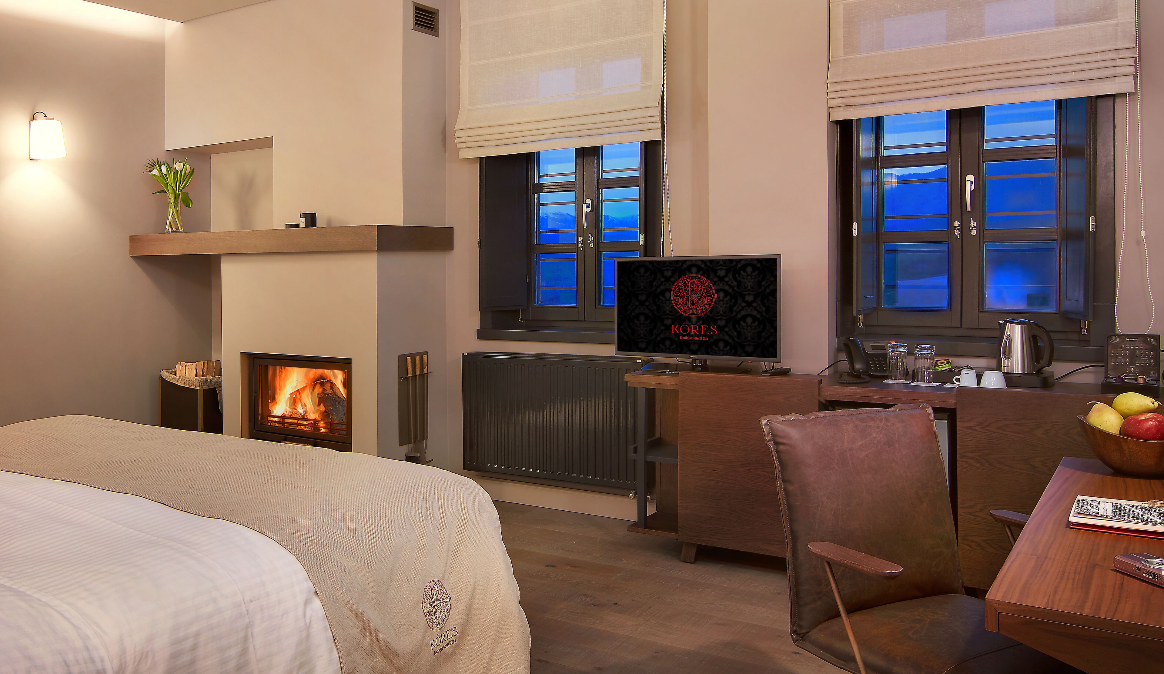 A hotel room with a bed, a TV, a fireplace, a desk, and a view of the outside.