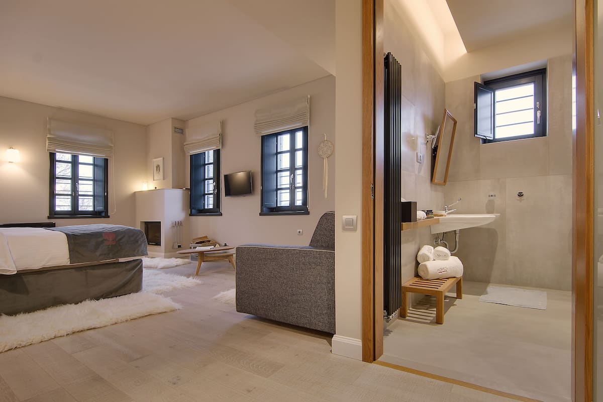 A modern bedroom with a bed, a sofa, a small table, and a bathroom with a sink and shower.