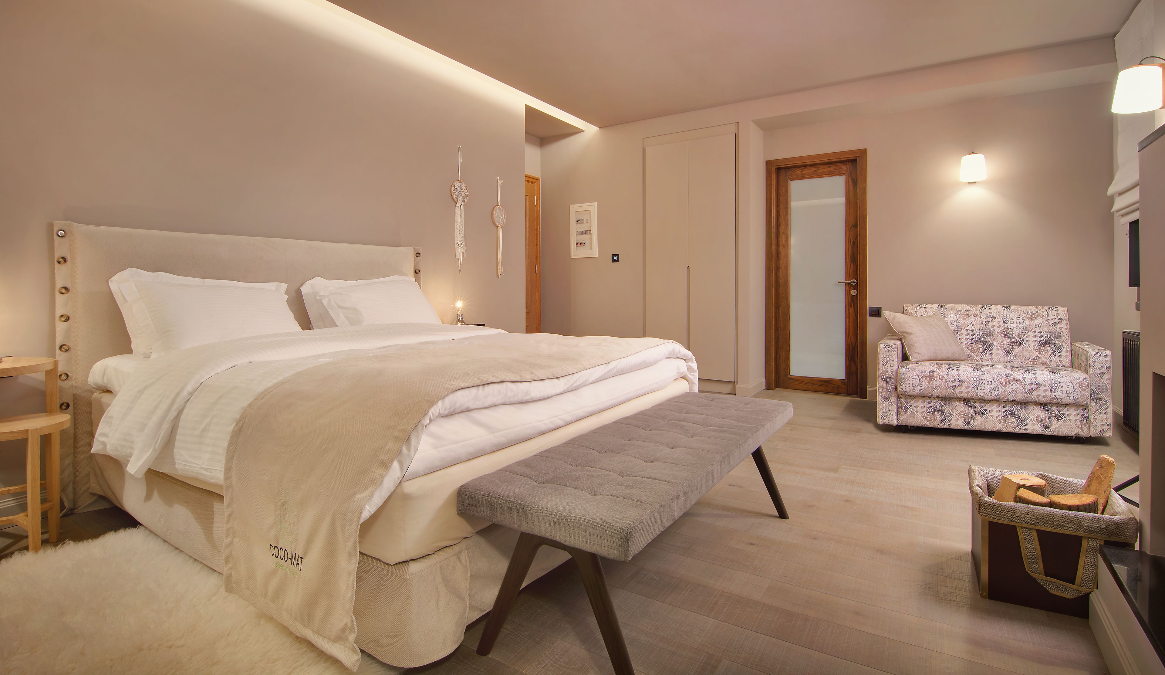 A bedroom with a bed, bedside table, bench, and a patterned armchair.
