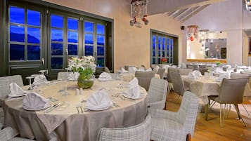 A restaurant with round tables set for dining, large windows, and a view of the outside.