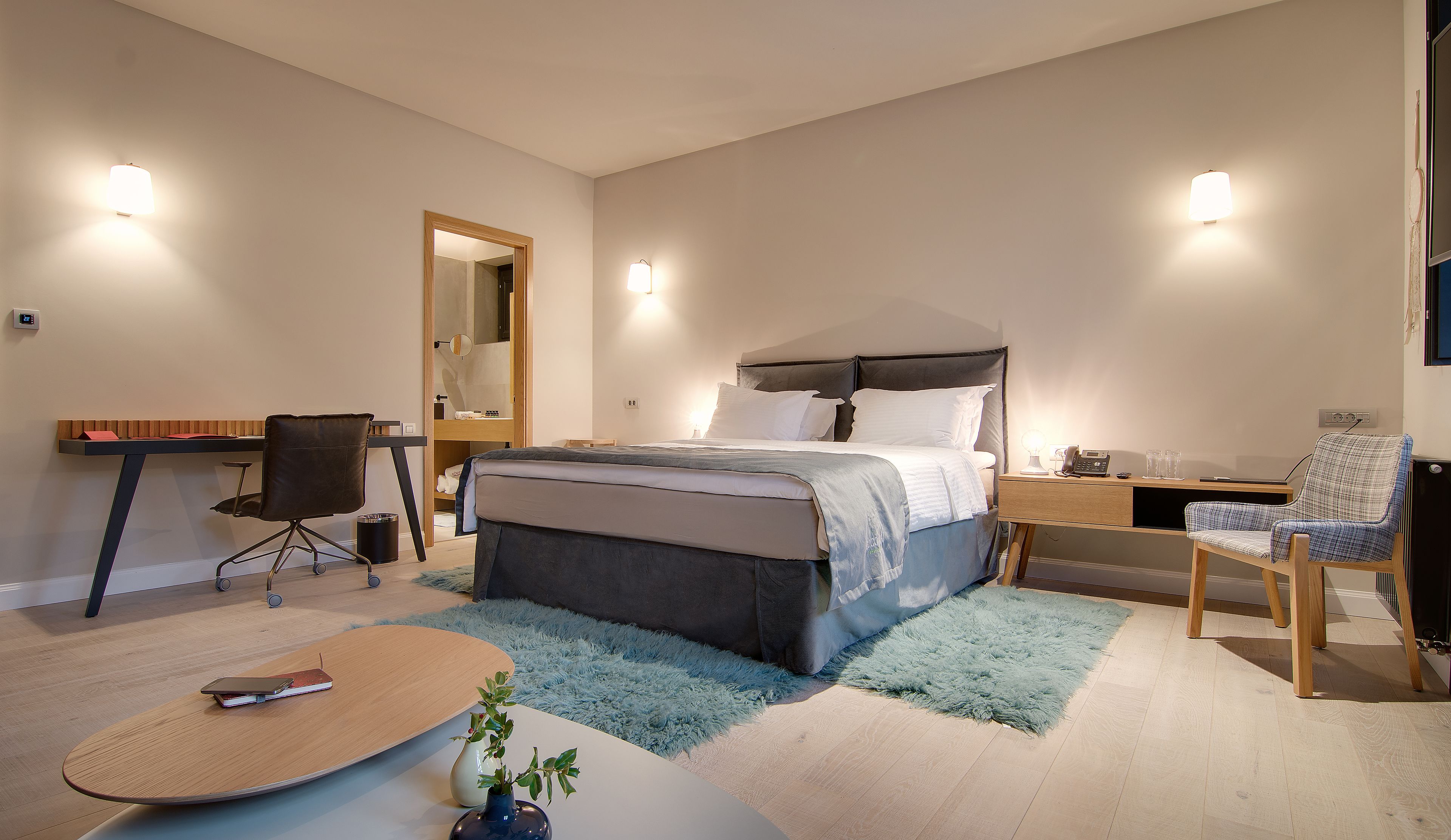 A modern bedroom with a bed, desk, chair, and a small table with a plant.