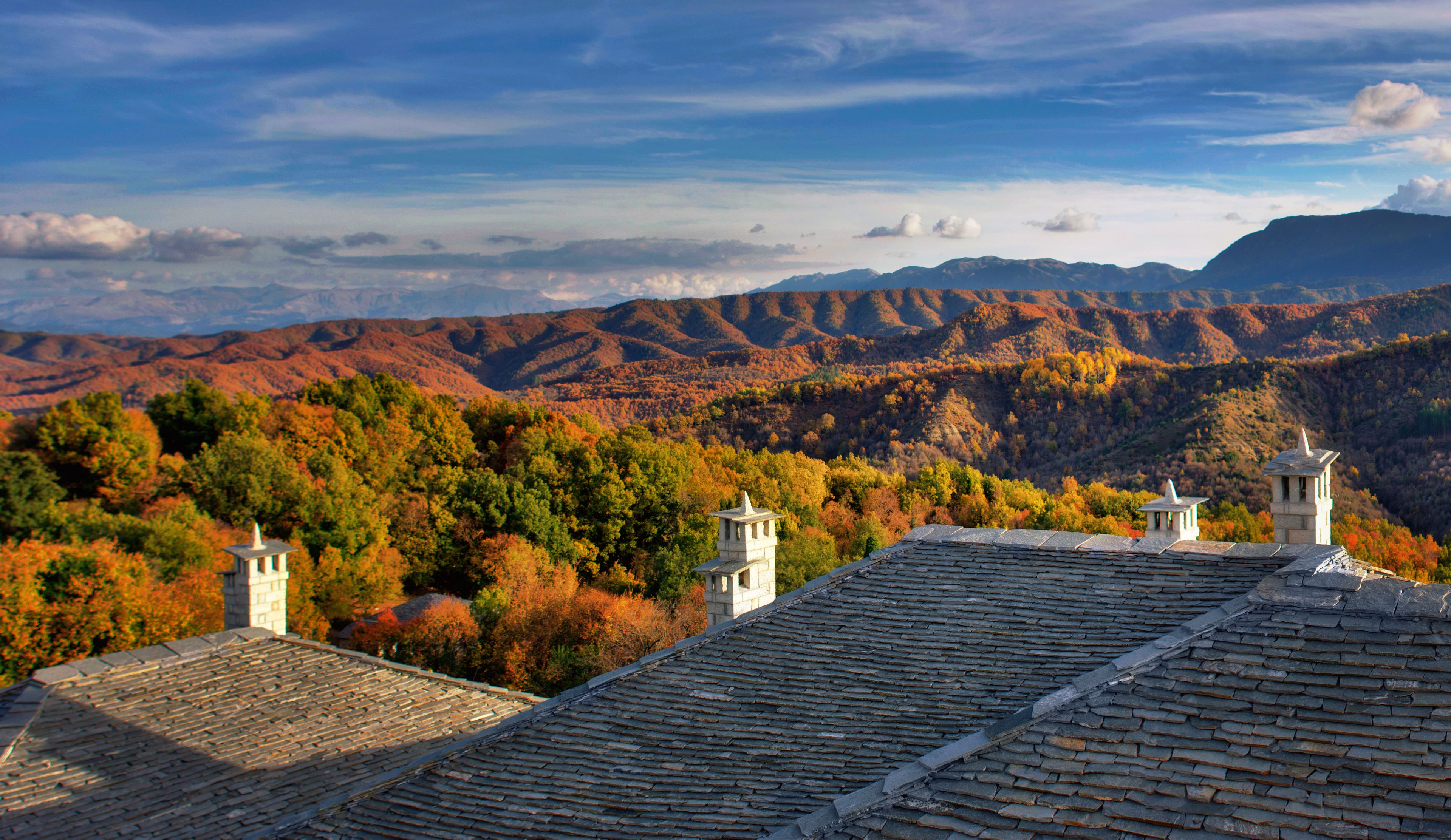 A view of a mountain landscape with autumn foliage and a building with a tiled roof and two towers.