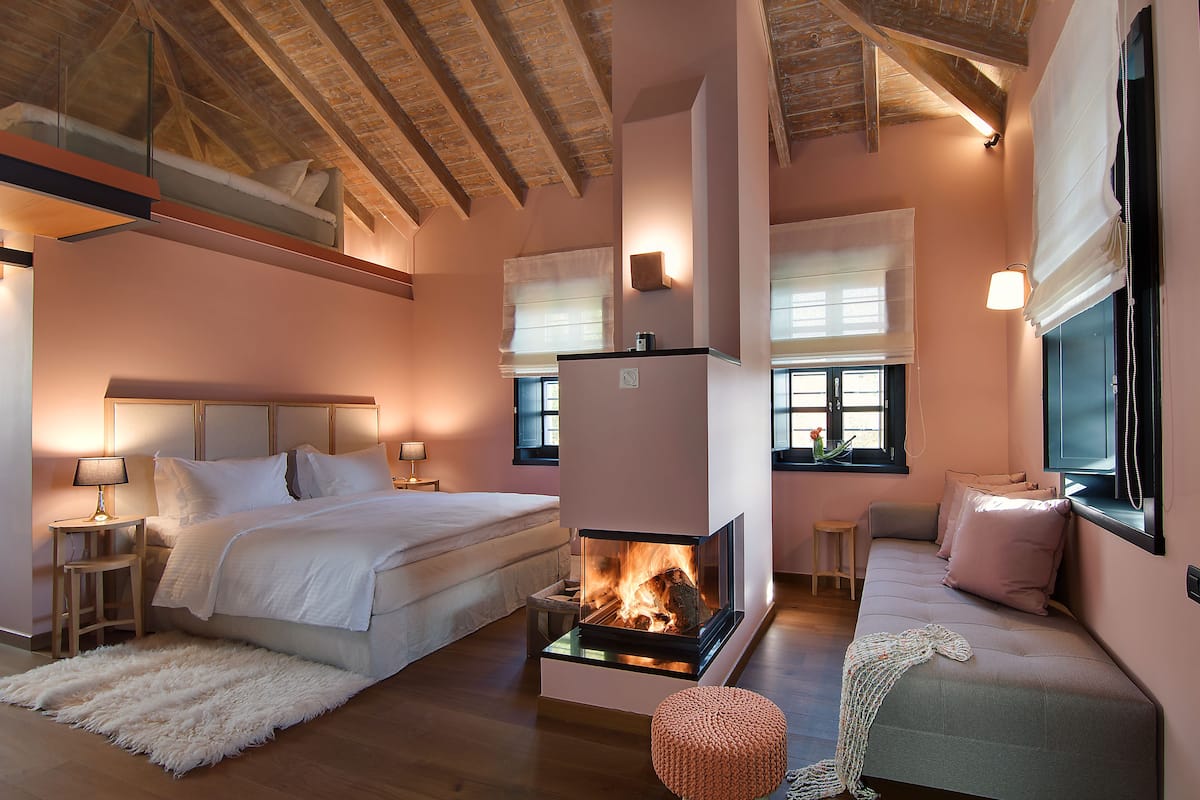 A cozy bedroom with a bed, bedside tables, a fireplace, and a seating area with a sofa.