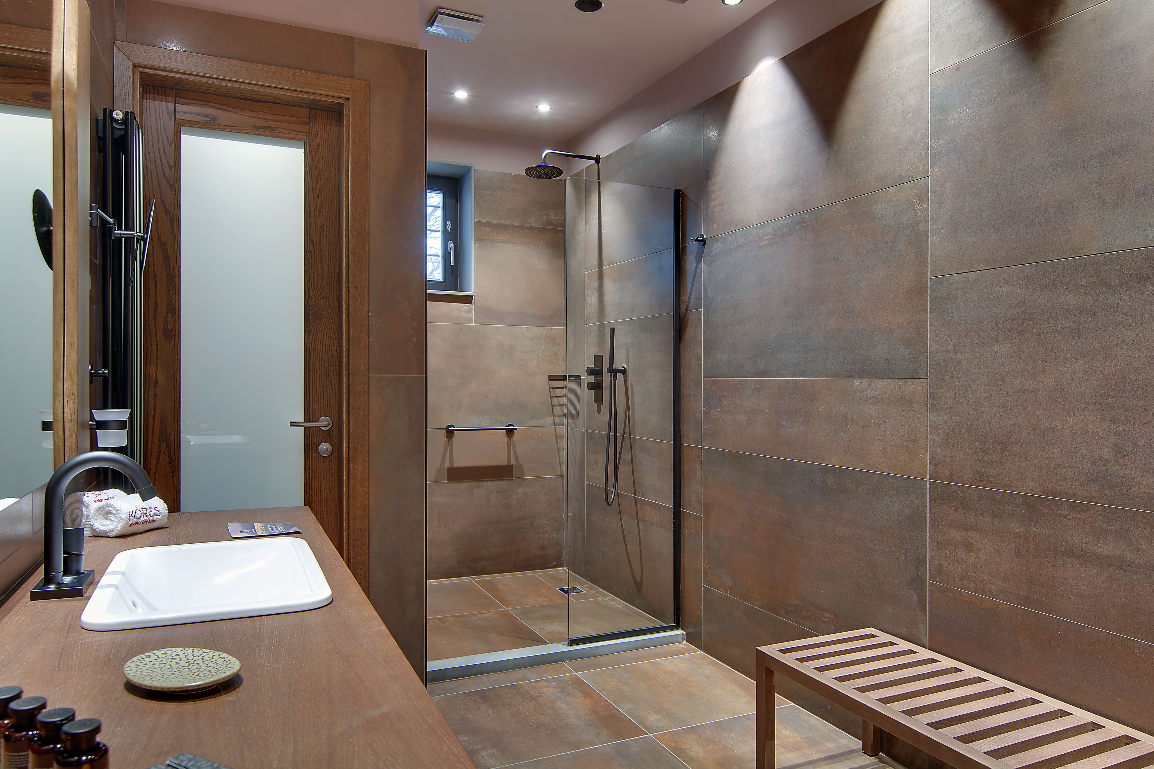 A modern bathroom with a glass-enclosed shower, a wooden vanity with a sink, and a bench.