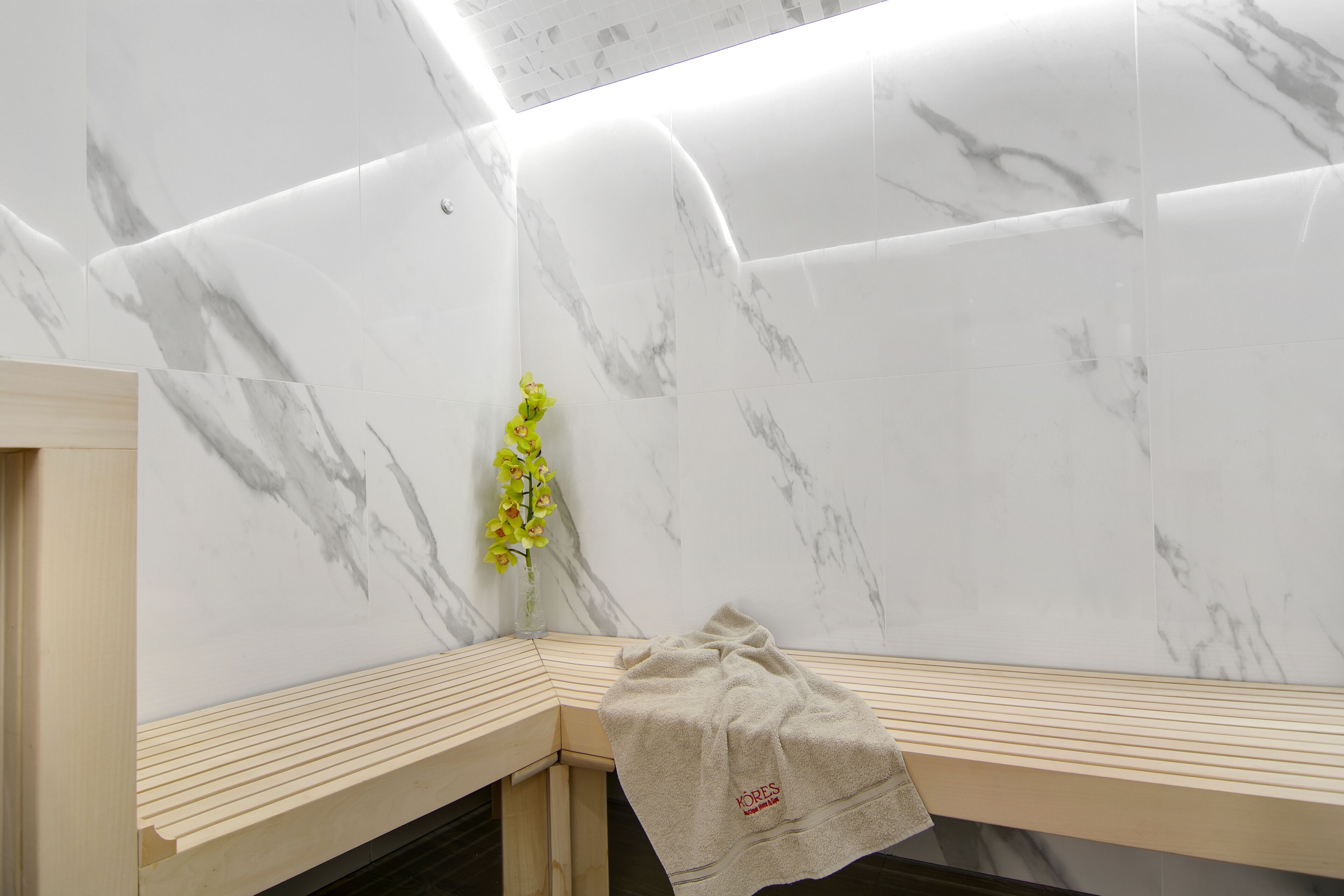 Un baño con paredes de mármol, un banco de madera y una toalla colgada en la pared.
