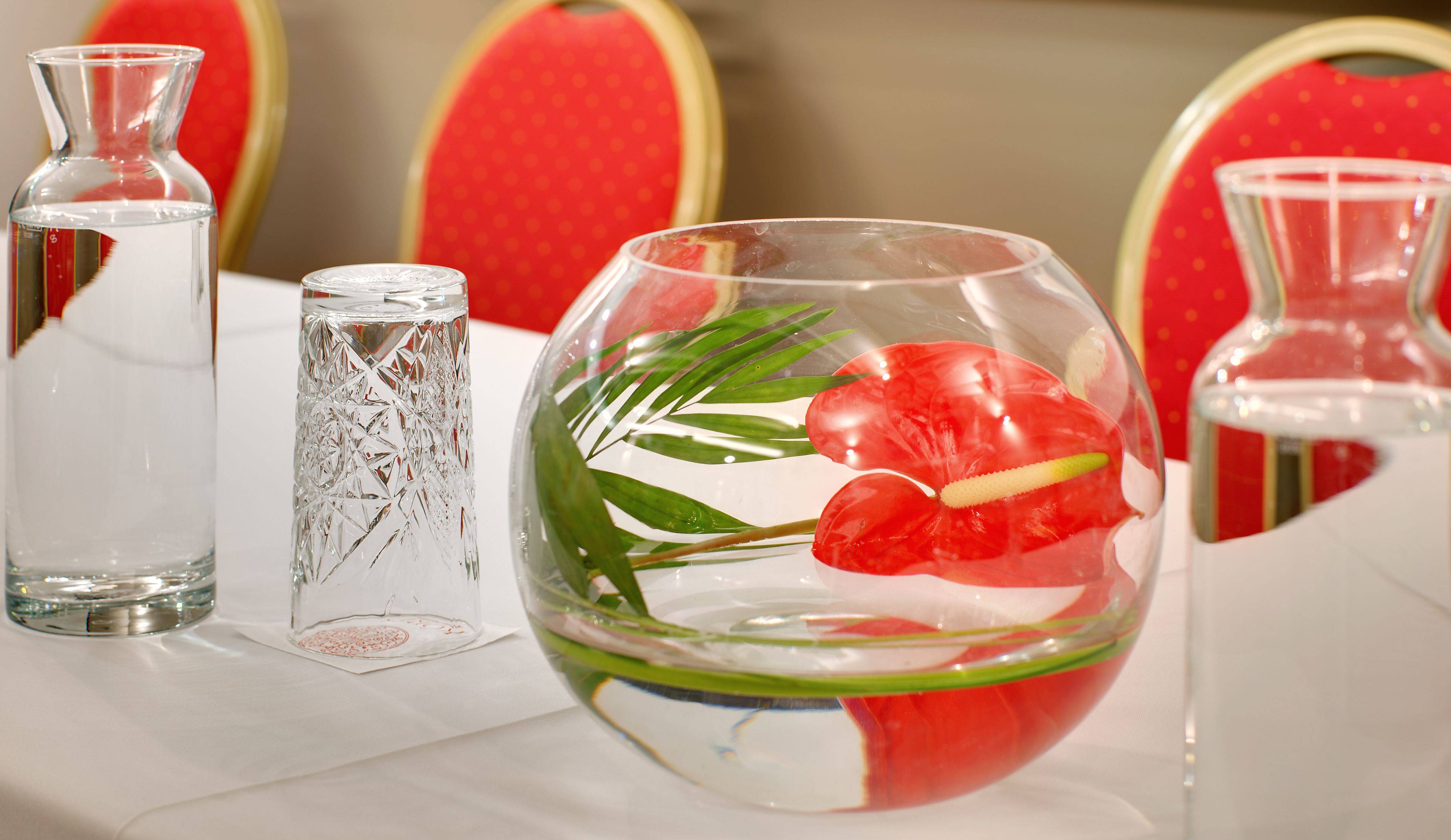 Una mesa con tres jarrones de vidrio transparente, uno con una flor roja y hojas verdes, y dos jarrones vacíos.